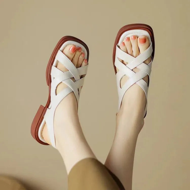 Women's glossy black patent leather sandals with a square toe and a cross-strap design on a low rubber sole.
