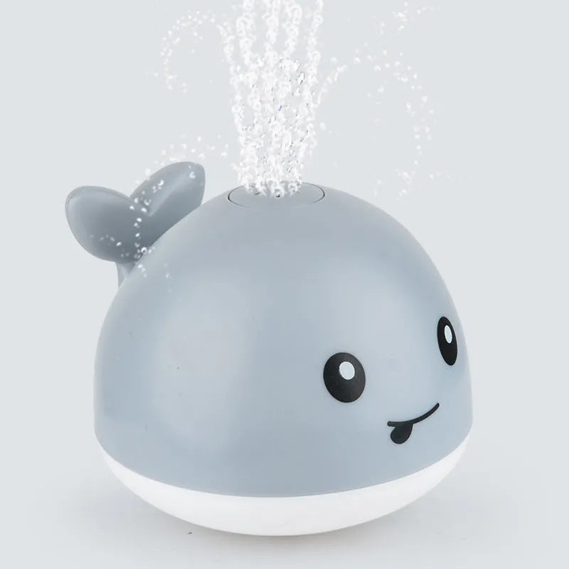 Automatic electric whale bath toy spraying water with LED lights on, floating in a baby bath.