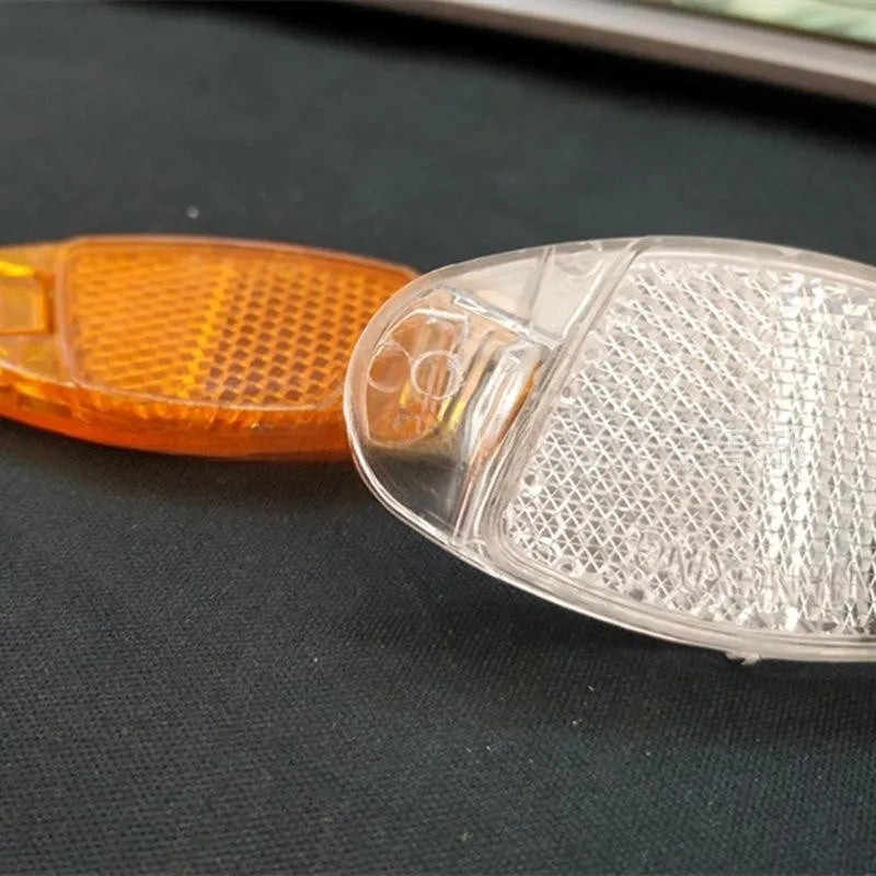 White and yellow plastic bicycle spoke reflectors measuring 7.2cm long by 3.5cm wide for night safety