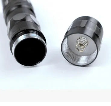 Black aluminium mini LED flashlight on a dark background, shown next to a AA battery for scale.