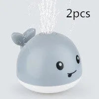 Automatic electric whale bath toy spraying water with LED lights on, floating in a baby bath.