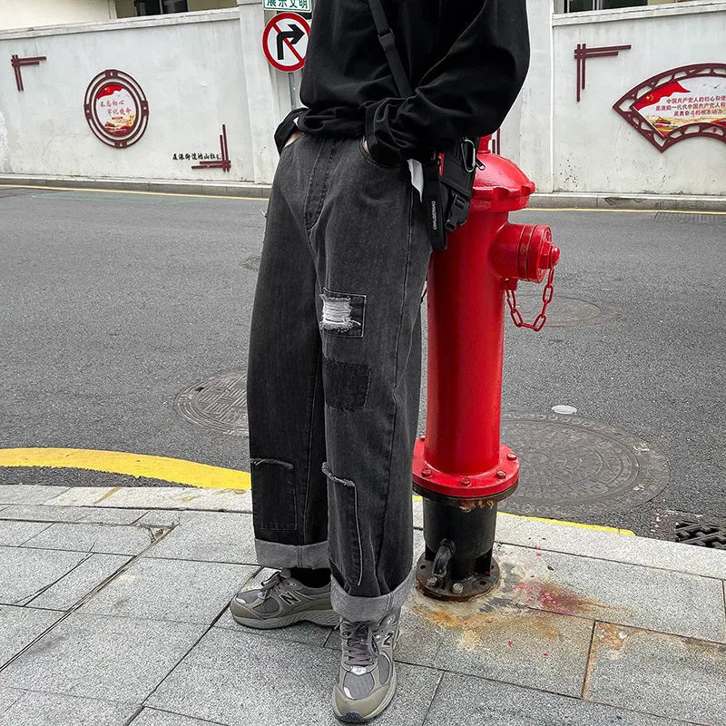 Men's high street ripped jeans with loose straight leg fit in black, showing rips on front thigh area