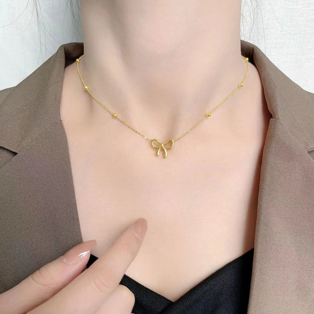 Gold electroplated titanium steel bow necklace on a cross chain, adjustable length.