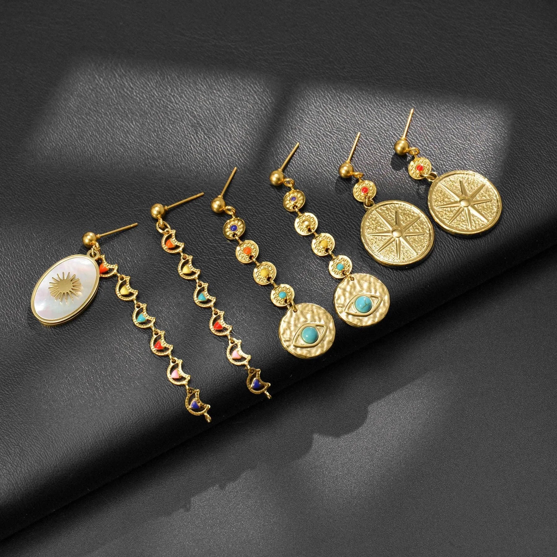 Three pairs of stainless steel geometry earrings: a star design, an eye design, and a shell sun design.