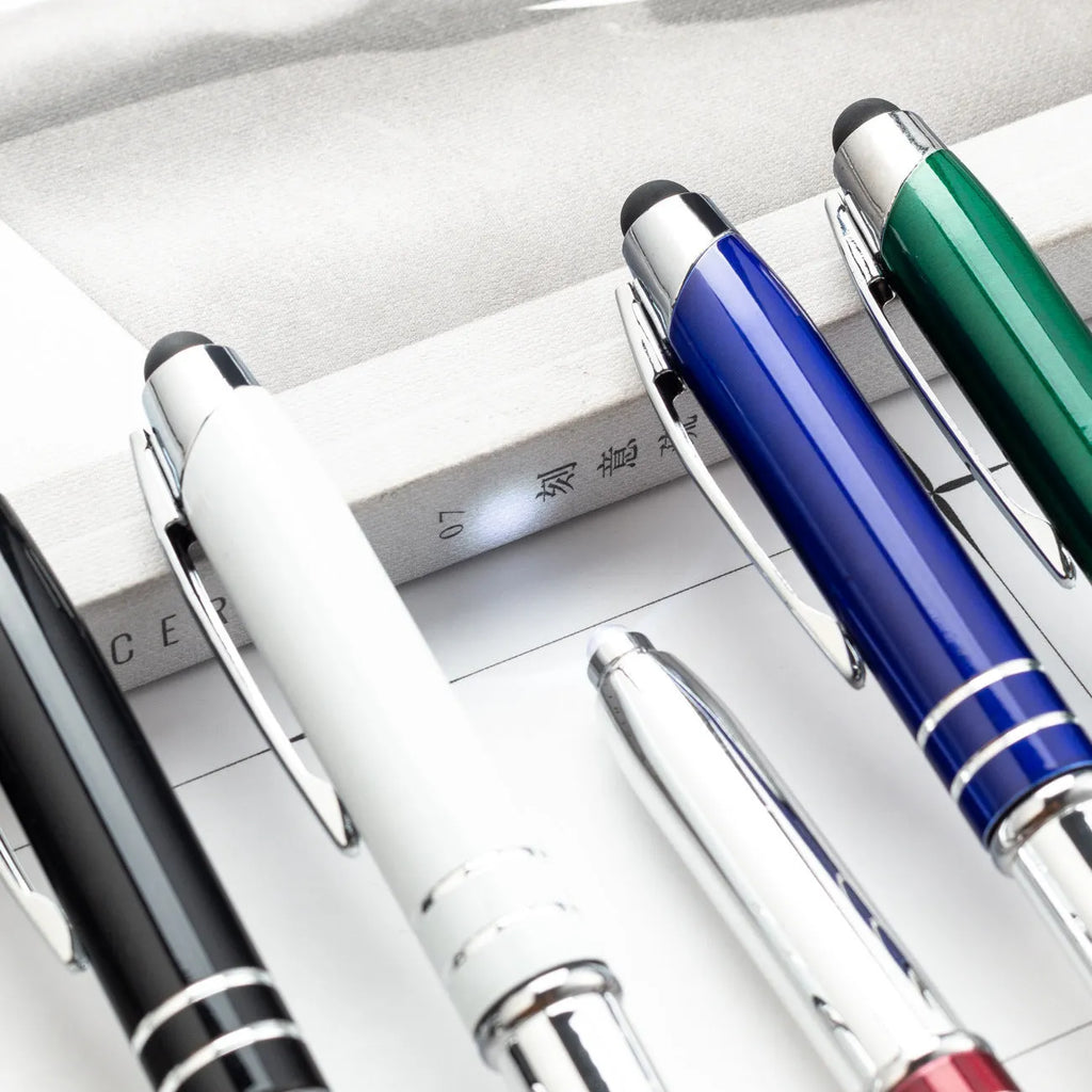 Red metal capacitive stylus and ballpoint pen with a built-in LED light on a desk next to a tablet.
