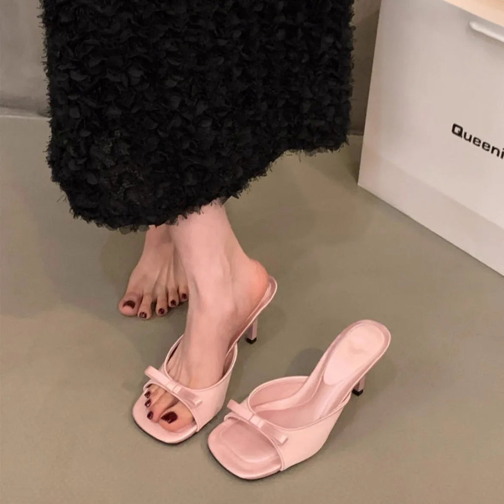 Square head fairy bow high heel slippers with ankle strap in beige on display.
