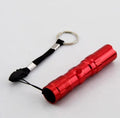 Black aluminium mini LED flashlight on a dark background, shown next to a AA battery for scale.