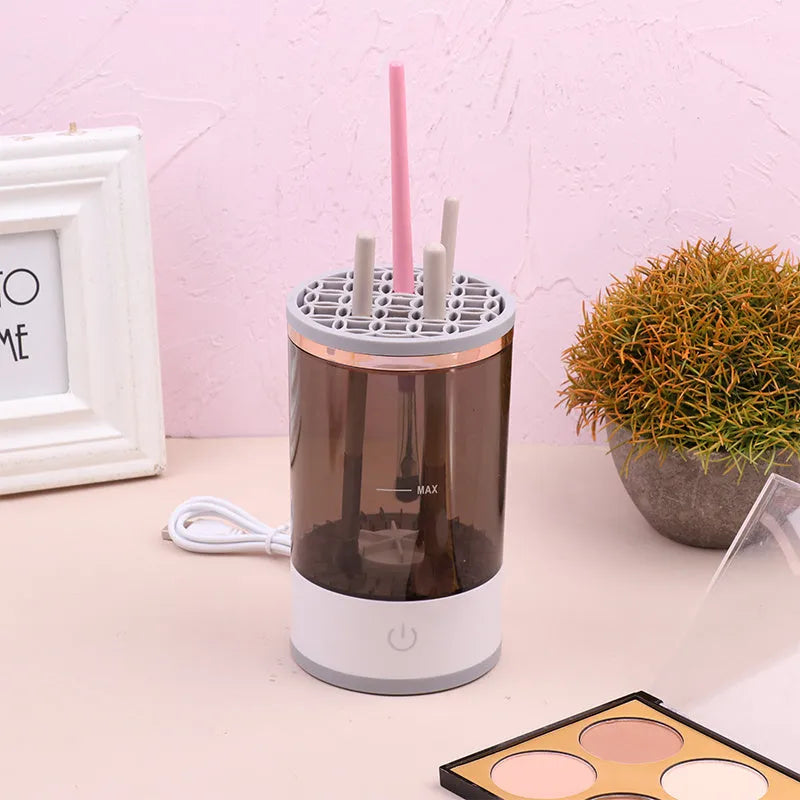 Grey and white electric makeup brush cleaner machine with USB cable on a white background