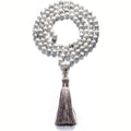 Long beaded agate and amethyst tassel necklace with geometric pendant on a neutral background.