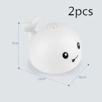 Automatic electric whale bath toy spraying water with LED lights on, floating in a baby bath.