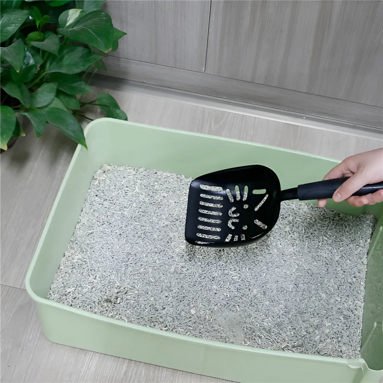 Alloy cat litter scoop with plastic handle on a cat litter box, showing cat face hole design for sifting.