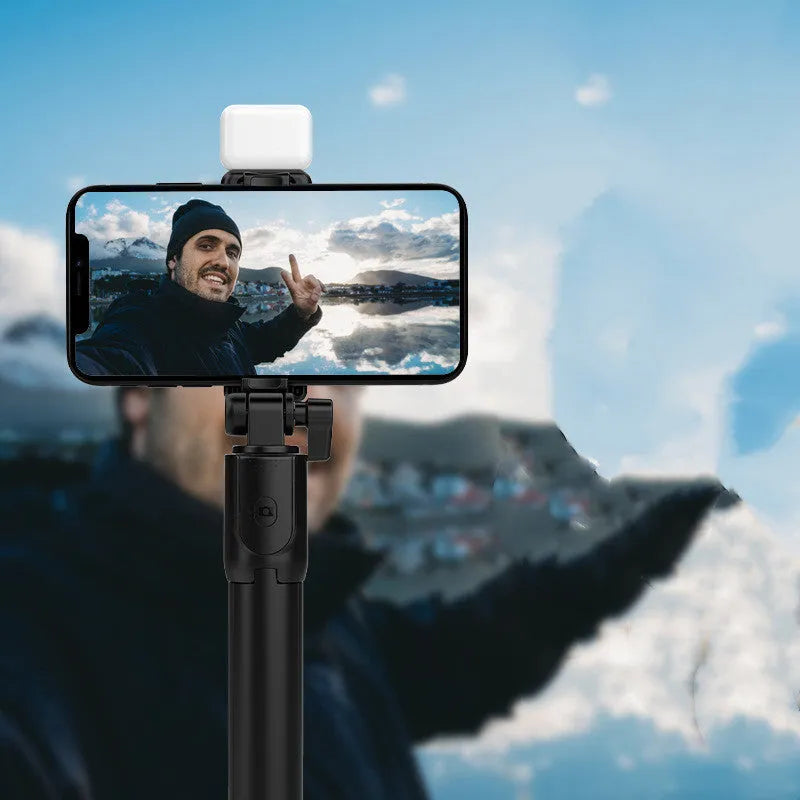 Black Bluetooth selfie stick with extended tripod legs holding an iPhone, showing its 360-degree rotating phone holder.