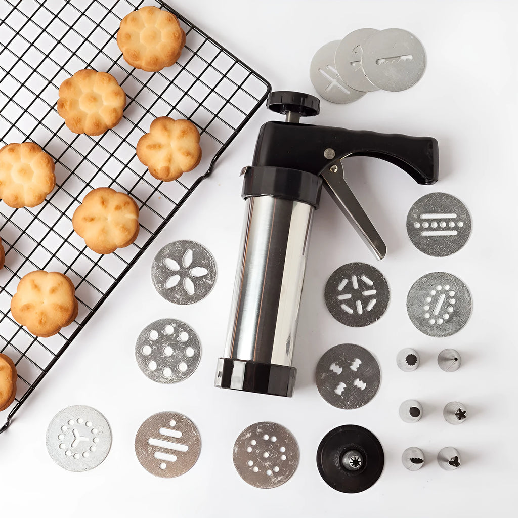 Stainless steel biscuit press gun with assorted cookie moulds and icing nozzles on a baking sheet.