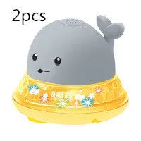 Automatic electric whale bath toy spraying water with LED lights on, floating in a baby bath.