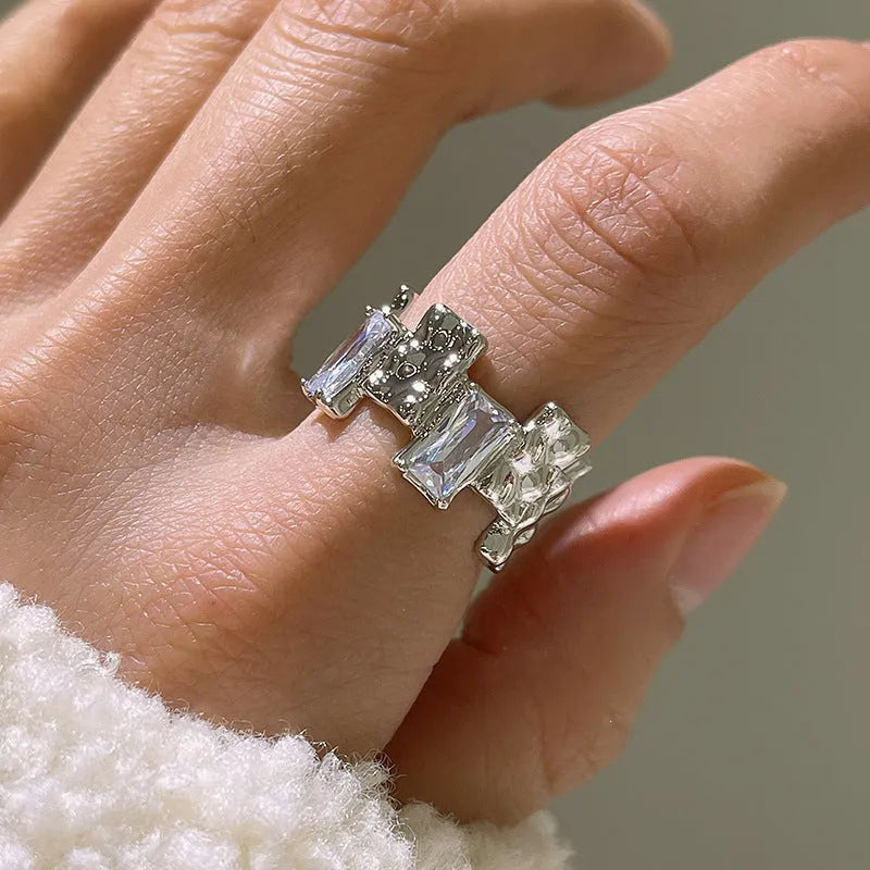 Silver plated open ring with a cross design and zircon gemstones in a geometric shape.
