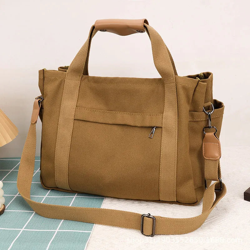 Horizontal square canvas tote bag in neutral colour with open zipper sides showing internal phone, document, computer and camera pockets