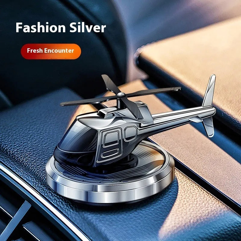 Silver metal solar-powered helicopter car ornament with rotating blades on a car dashboard.