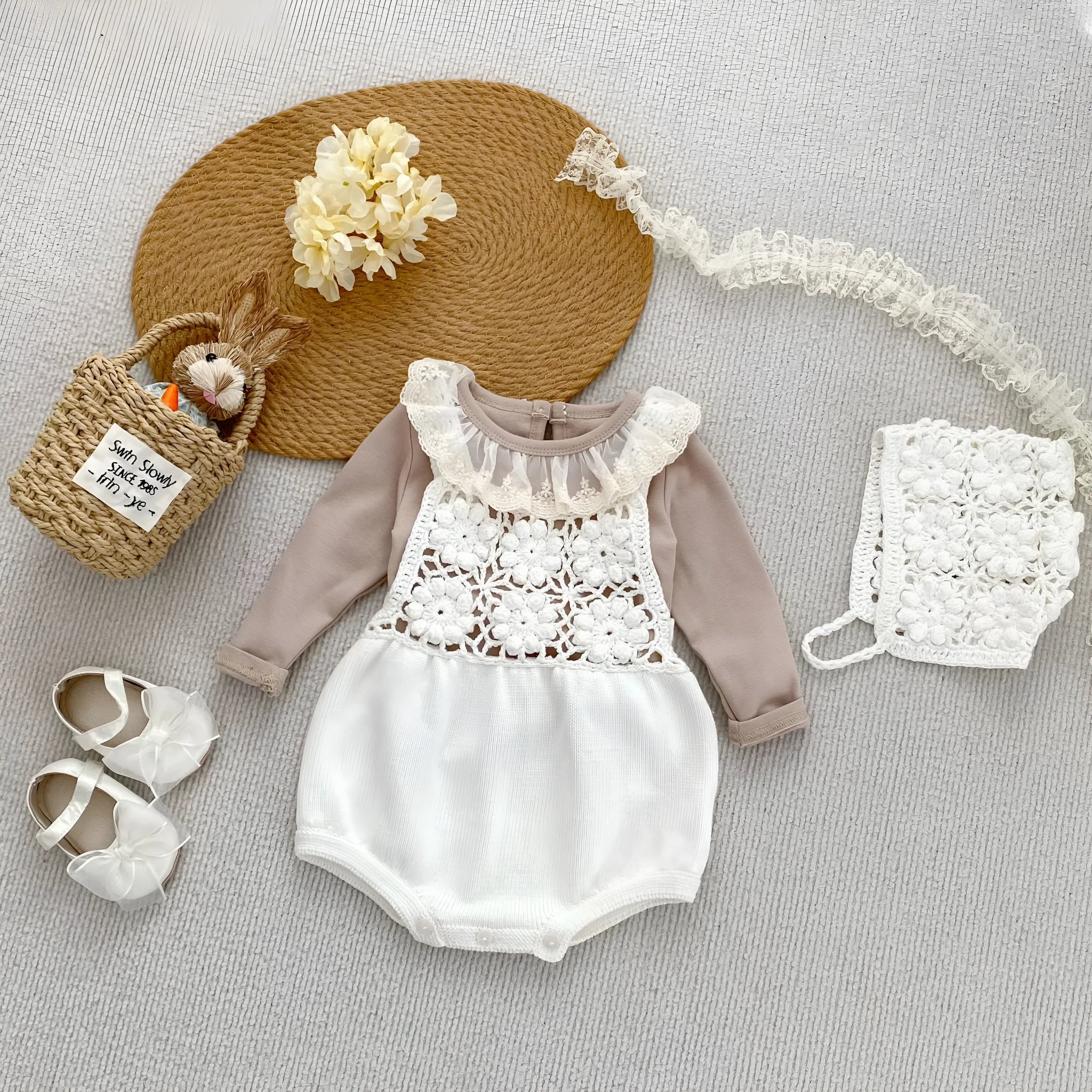 Beige baby romper with flower cutout strap and matching hat on a baby girl