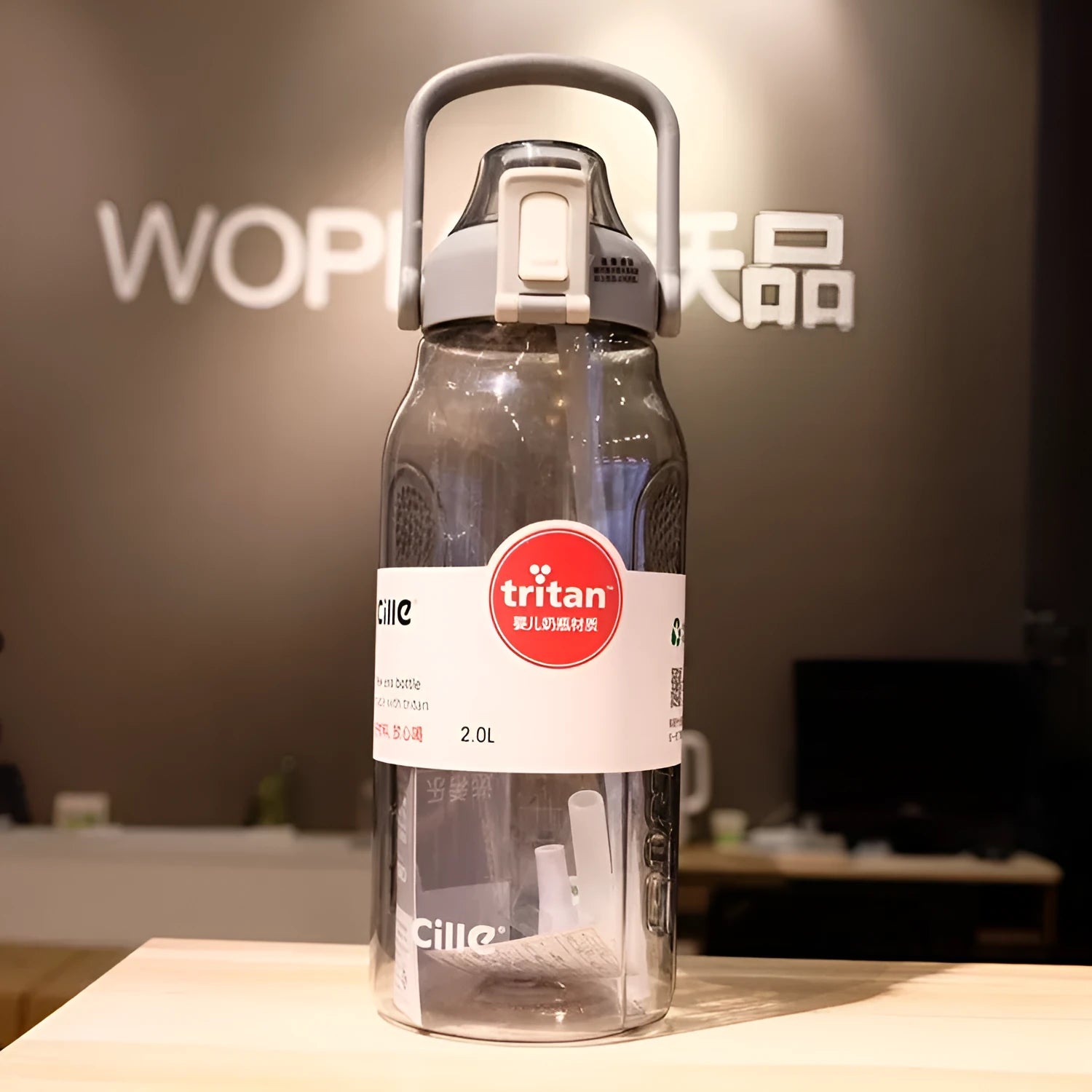 Grey plastic water bottle with black cap and clear straw showing scale markings on the side