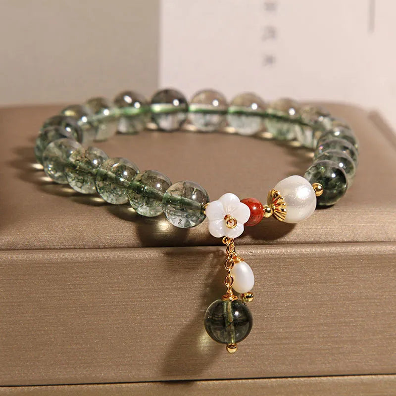 Green phantom quartz crystal bracelet with a silver shell flower charm on a model's wrist.