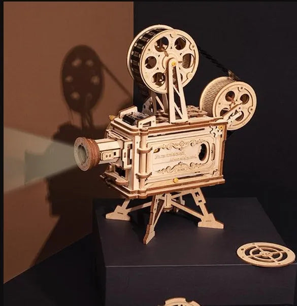Flat-packed wooden 3D puzzle film projector with visible gear wheel assembly and hand crank