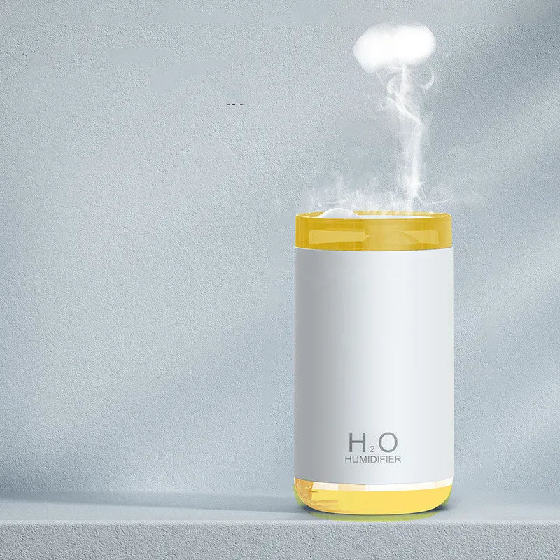 Blue jellyfish-shaped USB humidifier emitting smoke ring mist with warm night light on, placed on a wooden desk.
