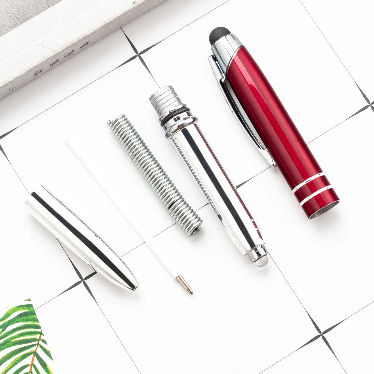 Red metal capacitive stylus and ballpoint pen with a built-in LED light on a desk next to a tablet.