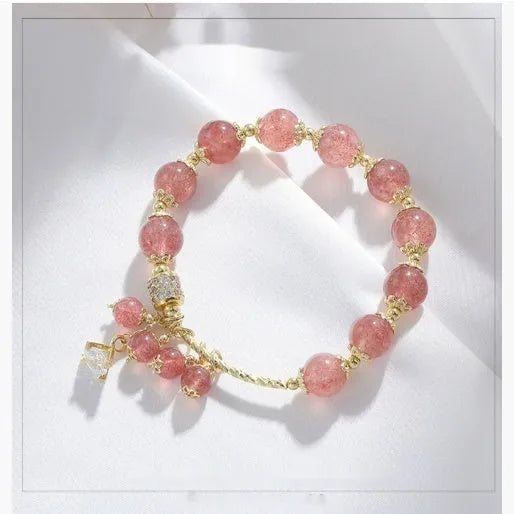 Close-up of a women's pink strawberry quartz crystal bracelet with heart-shaped beads and pearl accents.
