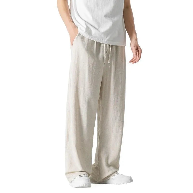 Man wearing beige straight-leg linen trousers with a drawstring waist, showcasing the cropped length and casual fit.