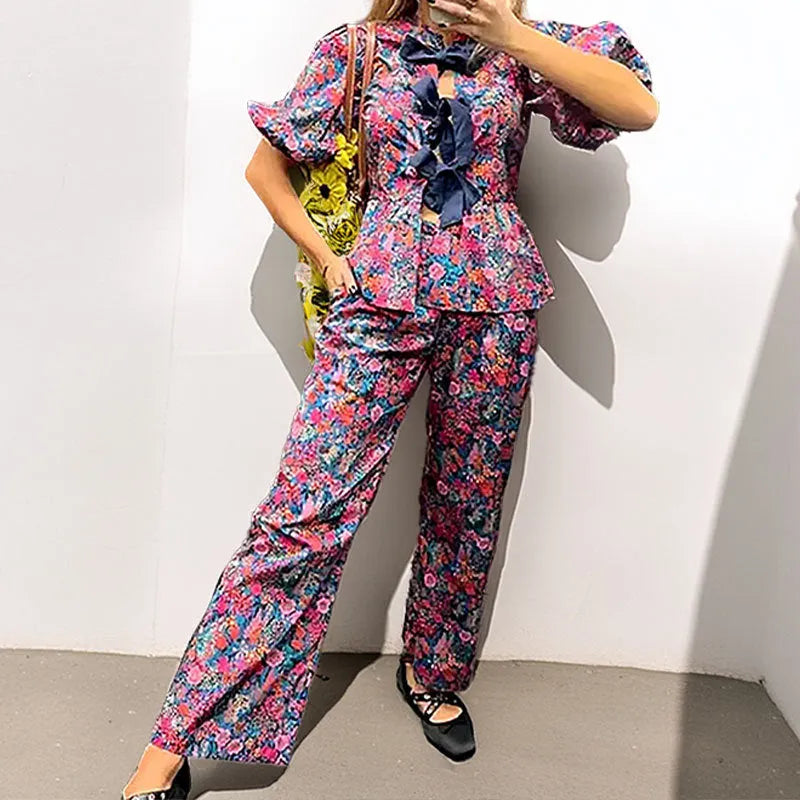 Women's floral print polyester trouser suit with puff sleeve blouse and matching trousers on a hanger.