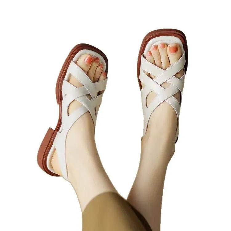 Women's glossy black patent leather sandals with a square toe and a cross-strap design on a low rubber sole.