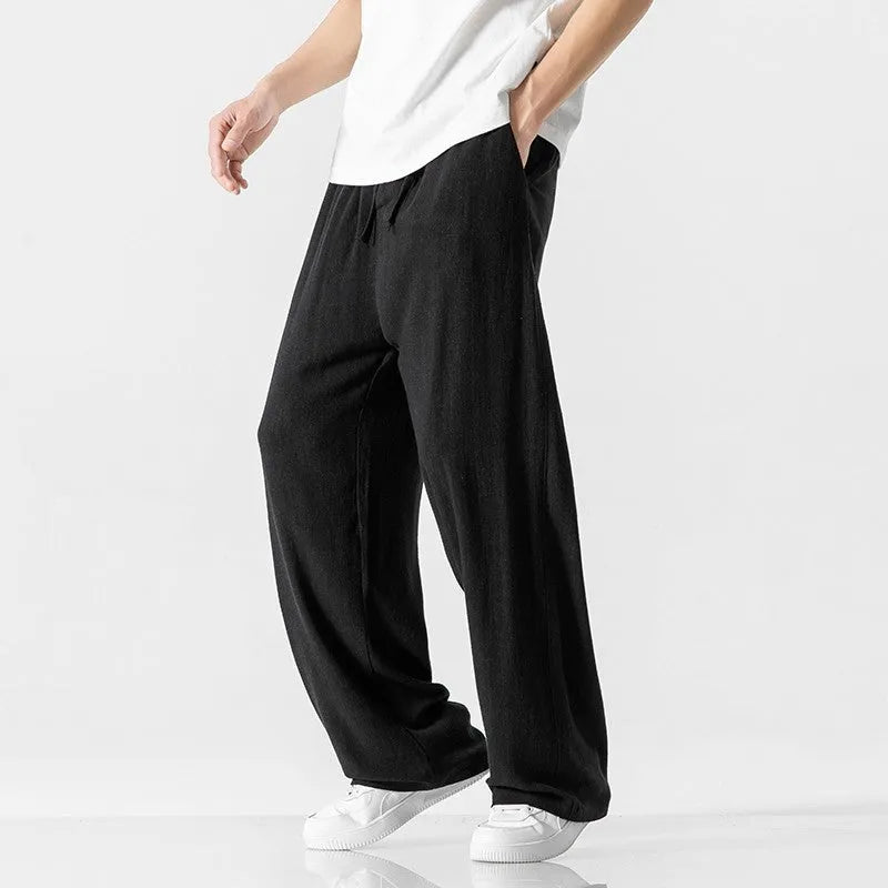 Man wearing beige straight-leg linen trousers with a drawstring waist, showcasing the cropped length and casual fit.