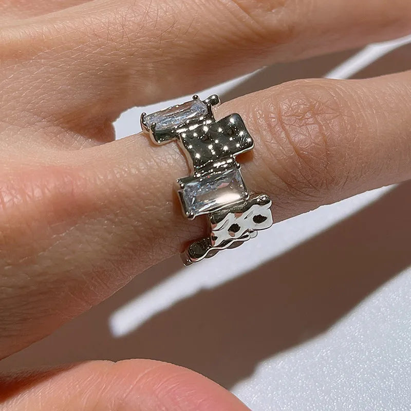Silver plated open ring with a cross design and zircon gemstones in a geometric shape.