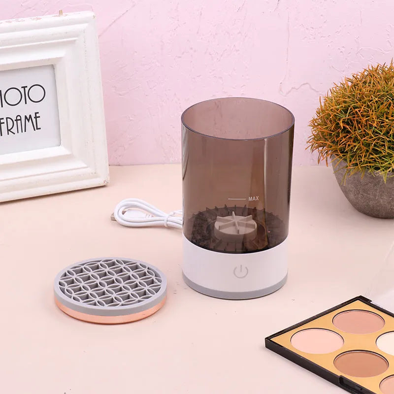 Grey and white electric makeup brush cleaner machine with USB cable on a white background