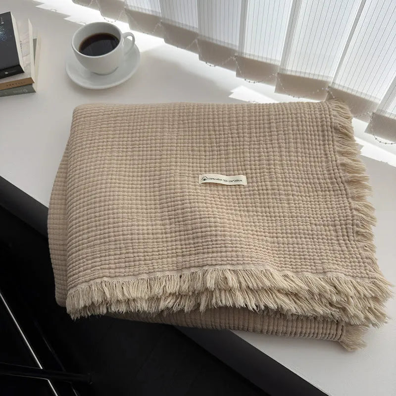 Soft cotton four-layer gauze throw blanket with tassel edges in navy blue, shown draped over a sofa.