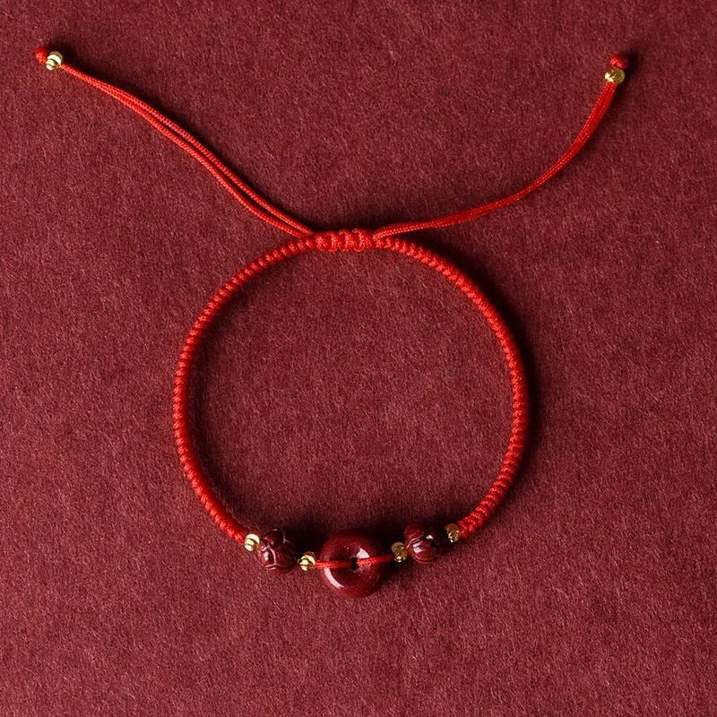 Close-up of a cinnabar heart charm on an adjustable black rope bracelet with a safety buckle.