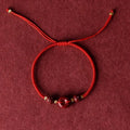 Close-up of a cinnabar heart charm on an adjustable black rope bracelet with a safety buckle.
