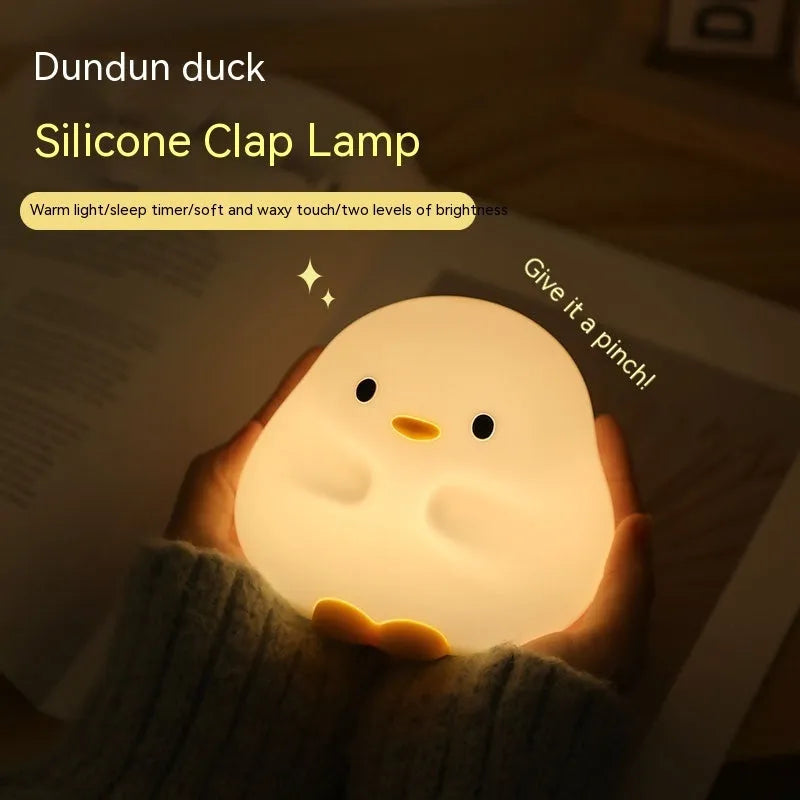 Cute duck shaped LED night lamp with silicone casing and warm light on a bedside table