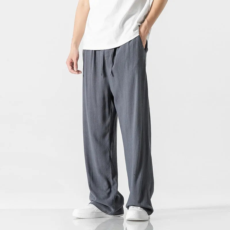 Man wearing beige straight-leg linen trousers with a drawstring waist, showcasing the cropped length and casual fit.