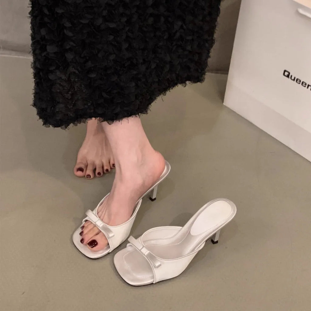 Square head fairy bow high heel slippers with ankle strap in beige on display.
