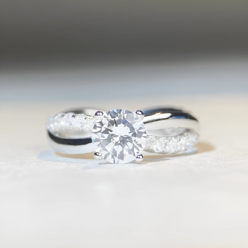 Geometric silver ring with a 1 karat moissanite in a four-claw setting, showing twisted band and cross design.