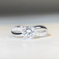 Geometric silver ring with a 1 karat moissanite in a four-claw setting, showing twisted band and cross design.