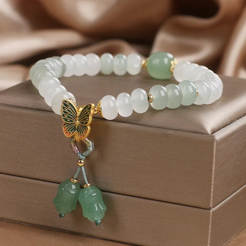 Green crystal abacus bead bracelet with a retro butterfly charm and tassels on a white background.