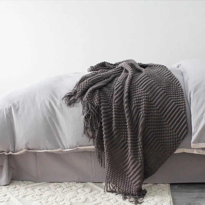 Small light grey polyester nap blanket folded on a sofa, showing its texture and size.