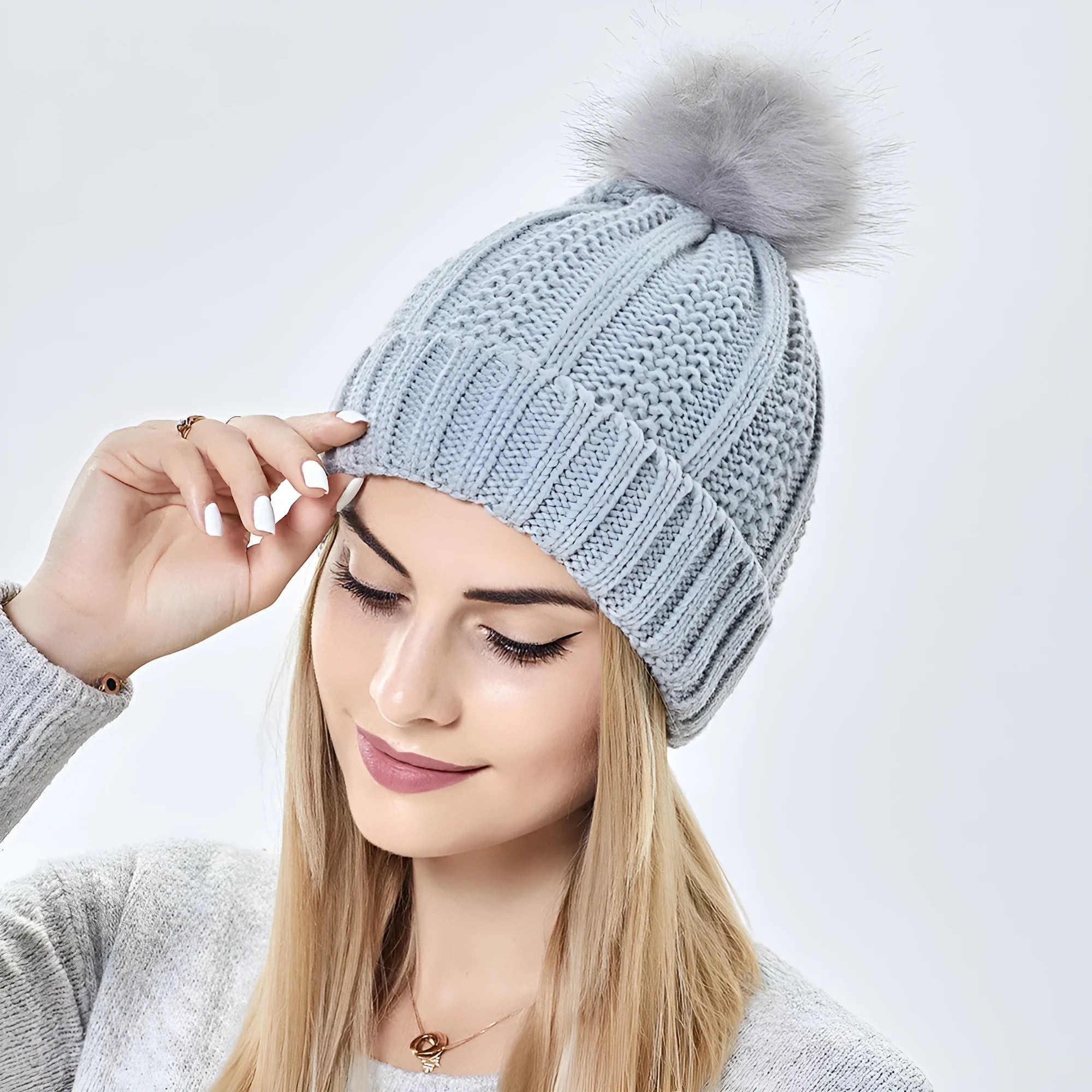 Women's black knit beanie hat with a white faux fur pom pom and satin lining for hair protection.