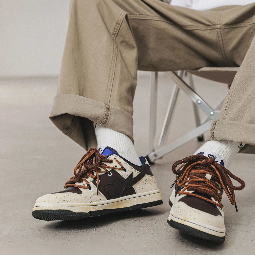 Brown low-top unisex casual sneakers with leather stitching, rubber sole, and front lace-up