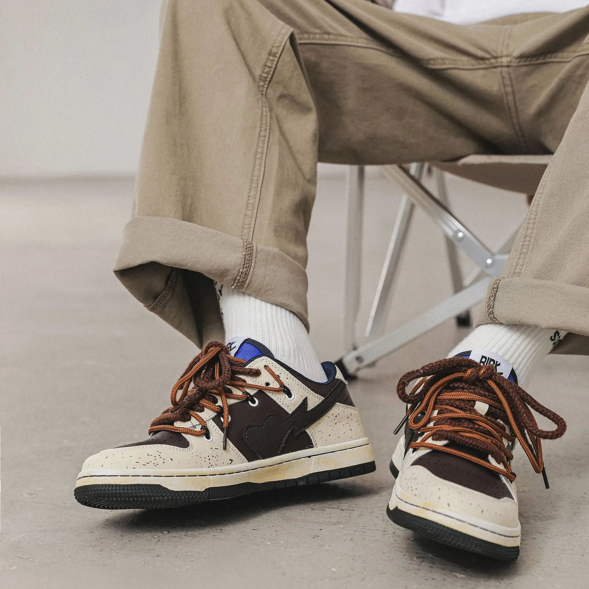 Brown low-top unisex casual sneakers with leather stitching, rubber sole, and front lace-up