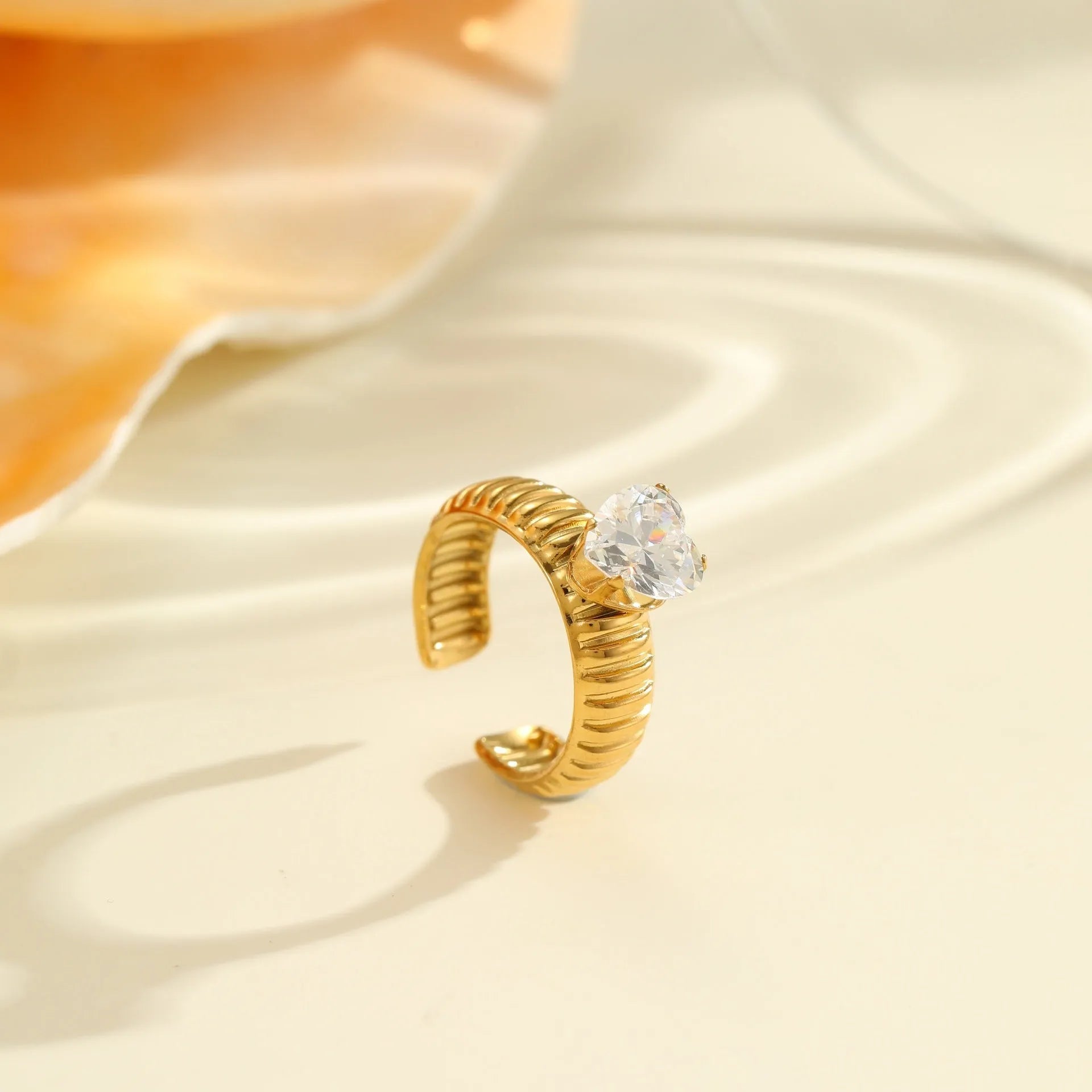 Gold electroplated stainless steel ring with zircon details in heart and geometric shapes on a grey background.