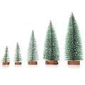 Set of artificial Christmas pine needle trees in green and white, heights 10cm to 30cm, on a tabletop