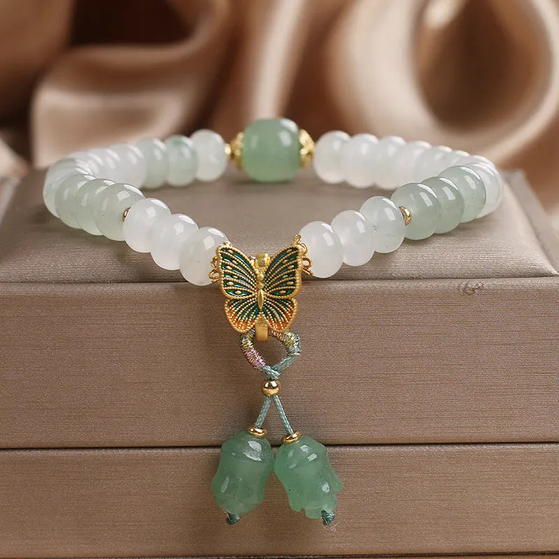 Green crystal abacus bead bracelet with a retro butterfly charm and tassels on a white background.
